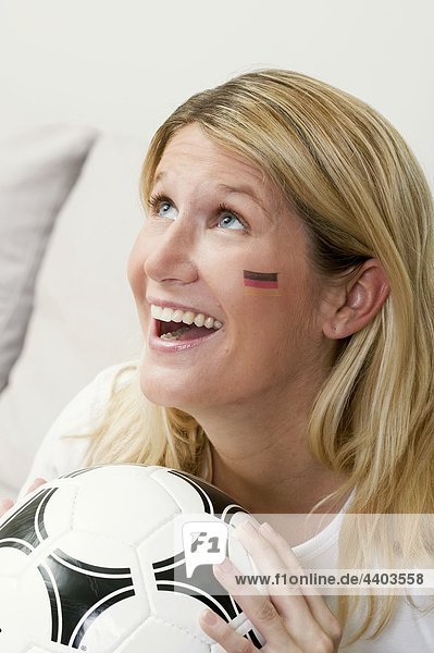 Junge Frau mit deutschen Farben auf ihrem Gesicht hält Fußball