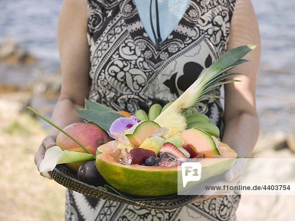 Woman holding tray of fresh exotic fruit by sea