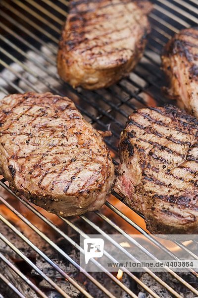 Several beef steaks on a barbecue grill rack