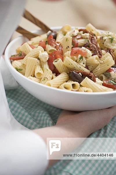 Frau hält Teller Pasta-Salat mit Oliven und Tomaten