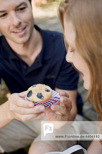 Man handing woman a blueberry muffin