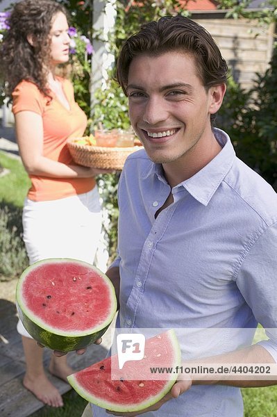 Junger Mann hält Watermelon  Frau mit Eistee im Hintergrund