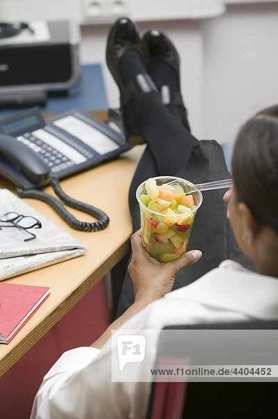 Frau isst Obstsalat im Büro