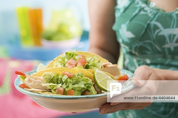 Frau hält Platte mit zwei Huhn tacos