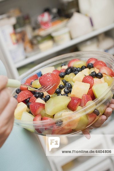 Frau Essen Obstsalat aus der Plastikschüssel an Kühlschrank