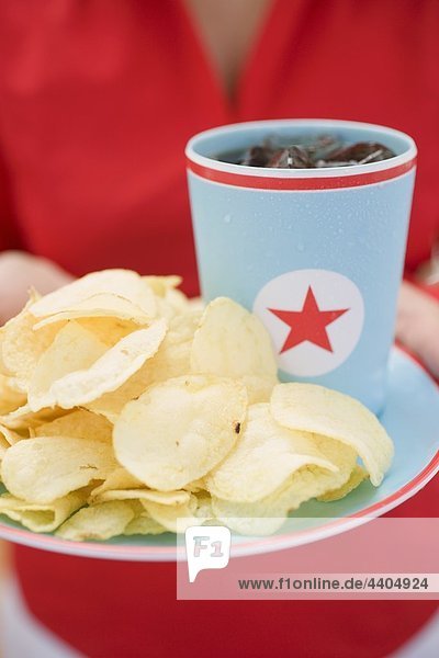 Frau hält Chips und Becherglas von Cola auf Platte