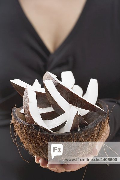 Frau hält Stücke Kokosnuss in ausgehöhlte Kokos