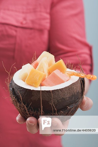 Frau hält ausgehöhlte Kokos voller exotischer Obstsalat