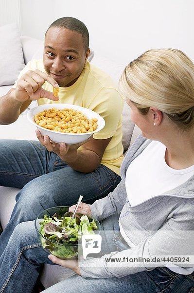 Paar auf Sofa mit Erdnuss Puffs und Salat