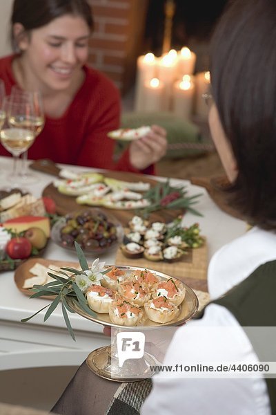 Two women eating appetisers in front of fireplace (Christmas)