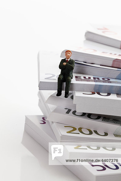 Managerfigur auf Euro-Banknotenstapel sitzend