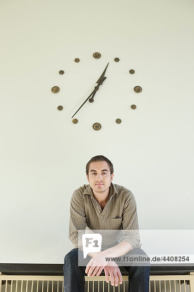 Mid adult man sitting against wall clock  portrait