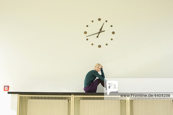 Young woman sitting against wall clock  portrait