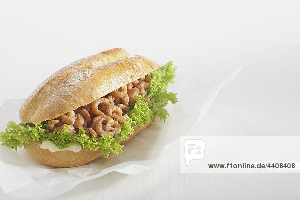 Baguette roll filled with shrimp against white background.