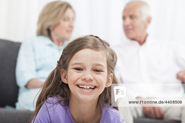Enkelin (6-7) lächelnd mit Großeltern im Hintergrund