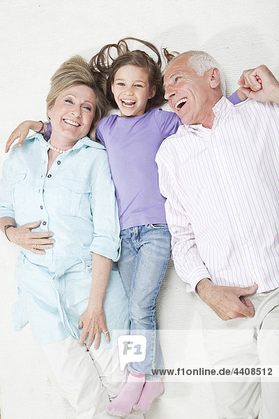 Enkelin (6-7) liegend mit Großeltern  lächelnd