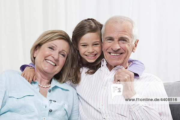Enkelin (6-7) Arm um Großeltern  lächelnd  Portrait