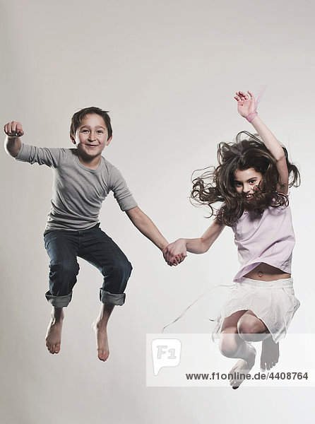 Boy and girl (8-9) holding hands and jumping  smiling  portrait