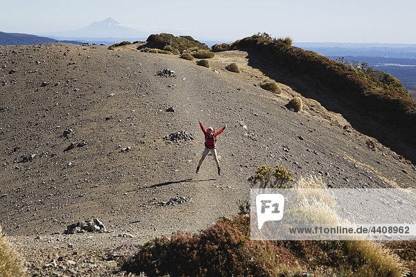 Neuseeland  Nordinsel  Frau springt auf Vulkanmoräne