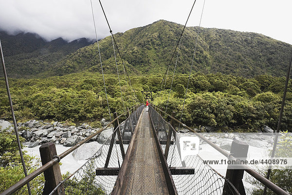 New Zealand  South Island  Woman crossing fox river through swing bridge