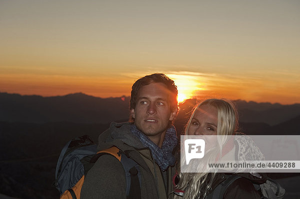 Österreich  Steiermark  Dachstein  Paar bei Sonnenuntergang auf Berggipfel stehend  lächelnd