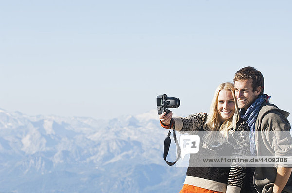 Österreich  Steiermark  Dachstein  Junges Paar fotografiert am Berg  lächelnd