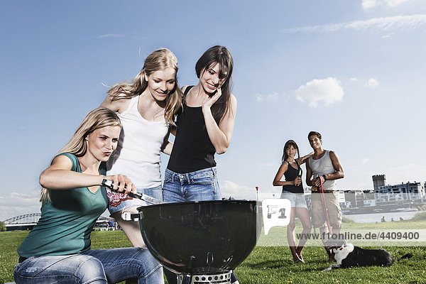 Women barbecueing and friends in background with dog