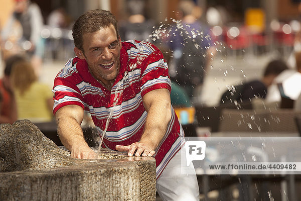 Man playing with fountain water  background people