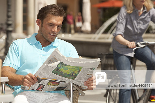 Man reading newspaper  person driving bicycle in background