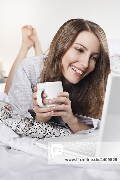 Woman lying on bed with laptop  smiling