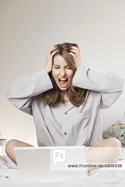 Woman with laptop and head in hand  shouting