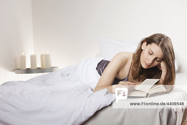 Vorne liegende Frau auf Bett und Lesebuch