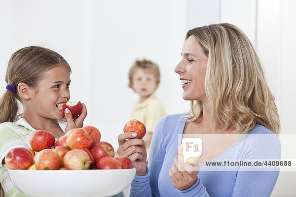 Mutter und Tochter essen Apfel mit Sohn im Hintergrund