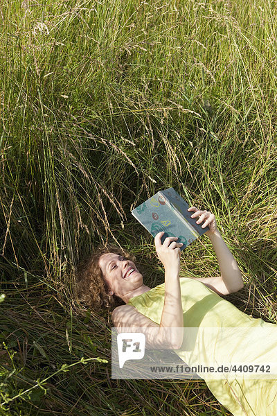 Frau auf Gras liegend und Buch lesend