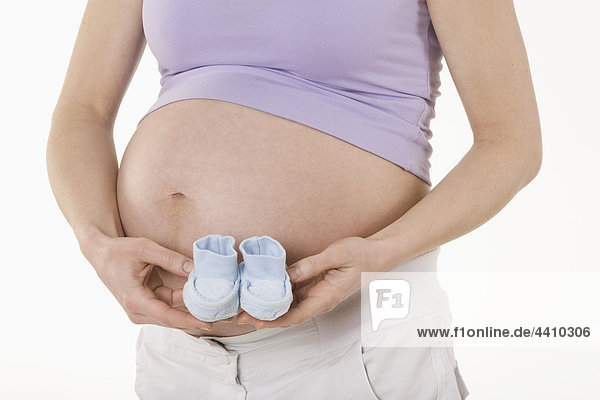 Schwangere Frau hält ein Paar Babysocken  Mittelteil