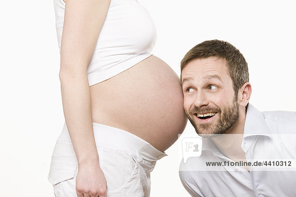 Mann  der dem Bauch einer schwangeren Frau lächelnd zuhört.