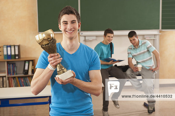 Junger Mann mit einer Trophäe mit Studenten im Hintergrund.