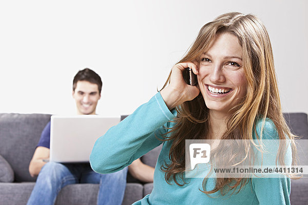 Woman talking on mobile phone  man using laptop in background