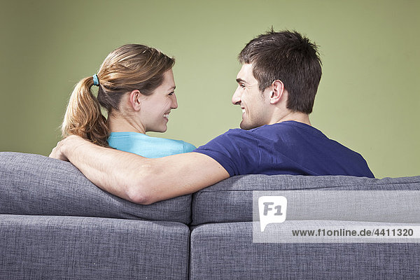 Junges Paar sitzt auf der Couch  lächelt sich an  Rückansicht
