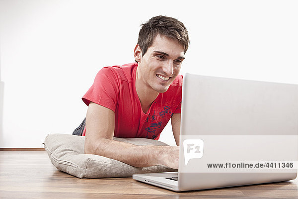 Young man lying on floor using laptop  smiling