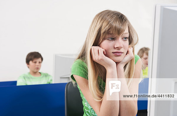 Teenage girl (14-15) with head in hand  boys using computer in background