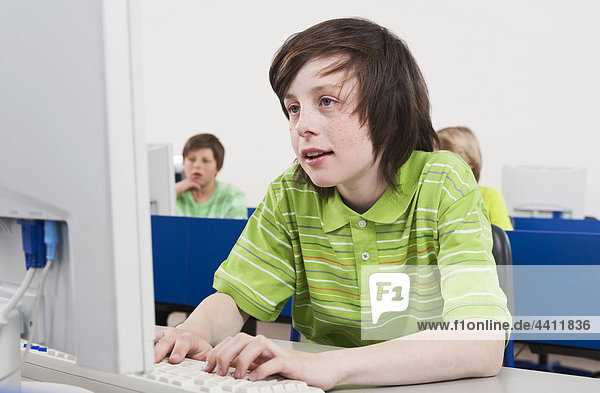 Boy (12-13) using computer with students in background