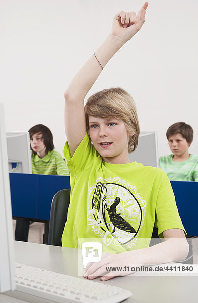 Teenage boy (14-15) hand raised with students using computer in background