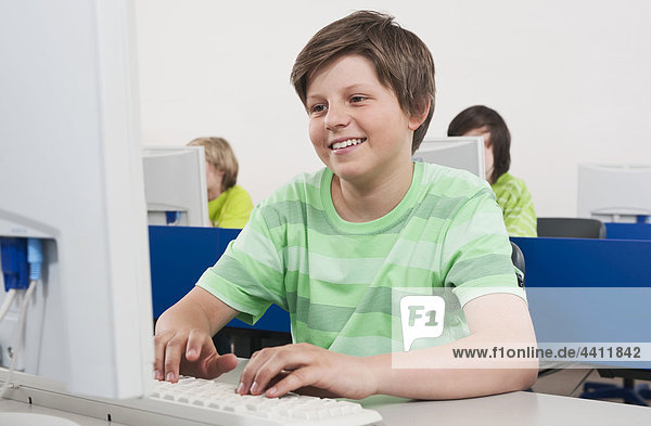 Boy (12-13) smiling and using computer students in background
