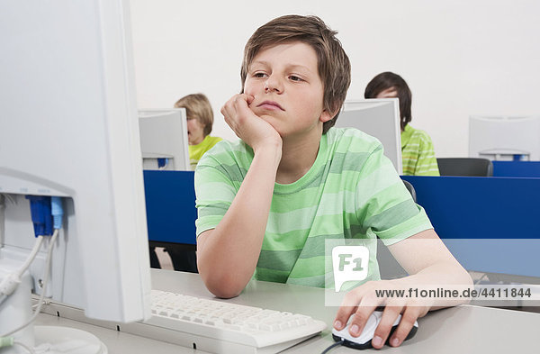 Boy (12-13) using computer with hand on chin and students in background