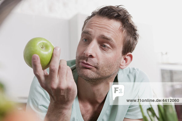 Deutschland  Mann beobachtet grünen Apfel  Nahaufnahme