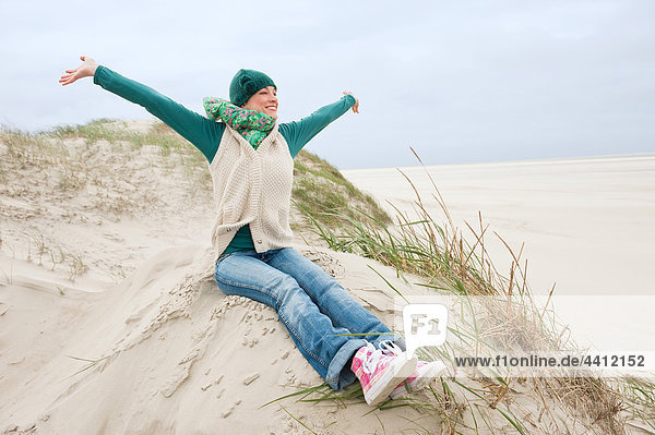 Germany  St Peter-Ording  North sea  Woman with arms up and having fun in sand dunes  smiling