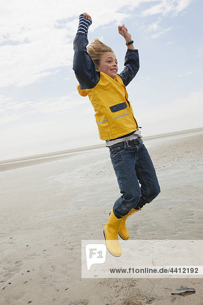 Nordsee  Junge (8-9) im Regenmantel am Strand springen