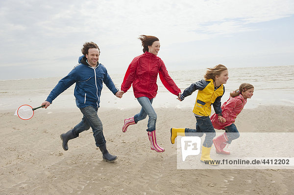 Germany  St. Peter-Ording  North Sea  Family holding hands and running on beach