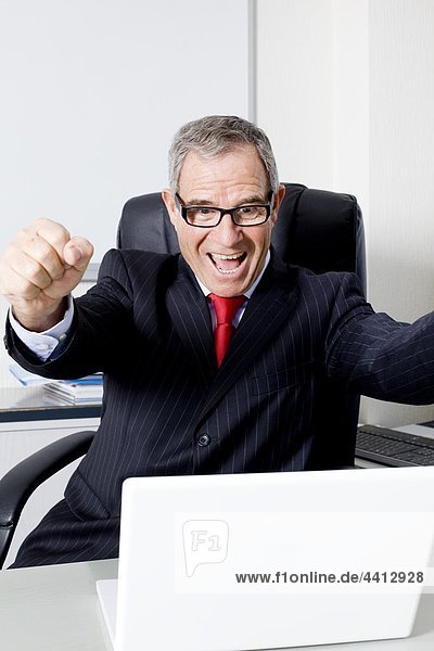 Businessman cheering in front of laptop